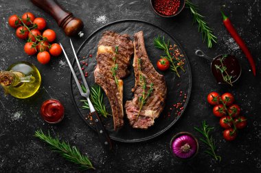 Kemiğe baharatlı iki dana biftek, kekik ve biberiye. Barbekü eti. Üst Manzara. Siyah taş kesme masasının üstünde düz bir görünüm vardı..