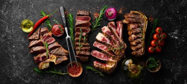 Biftek menüsü. Siyah taşlı arka planda dilimlenmiş biftekler: t-bone, striploin, kaburga, New York bifteği. Üst Manzara. Kırsal biçim.