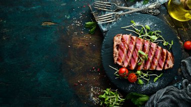 Siyah taş tabakta sebzeli sulu ton balığı bifteği pişirdim. Restoran yemeği. Deniz ürünleri. Kırsal tarzda. Düz Yat.