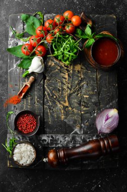 Mutfak mutfağı: kiraz domatesleri, soğanlar, baharatlar ve otlar. Siyah bir arkaplanda.