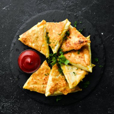 Asya yemekleri. Samsa, tavuk ve peynirli, ketçaplı, siyah taştan bir tabakta. Kırsal tarzda. Üst görünüm.