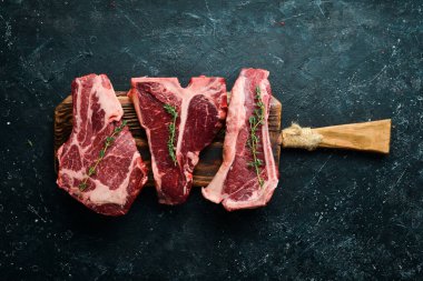 Çiğ biftek seti - T-bone, tomahawk, striploin, fileto, New York bifteği. Siyah taştan bir arka planda. Üst görünüm.