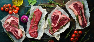 Çiğ biftek seti - T-bone, tomahawk, striploin, fileto, New York bifteği. Siyah taştan bir arka planda. Üst görünüm.