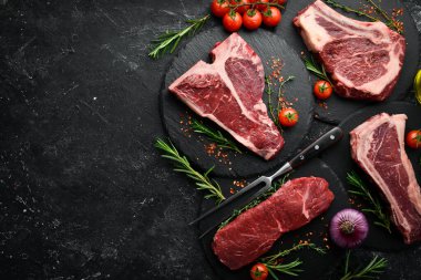 Çiğ biftek seti - T-bone, tomahawk, striploin, fileto, New York bifteği. Siyah taştan bir arka planda. Üst görünüm.