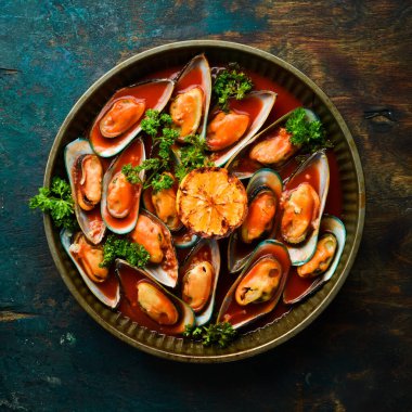 Domates sosunda sarımsak, maydanoz ve limonla pişirilmiş midye tepsisi. Siyah taştan bir arka planda.