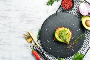 Sandviç: ciabatta, avokado, humus ve mikroyeşil. Kahvaltıda. Siyah taştan bir tabakta.