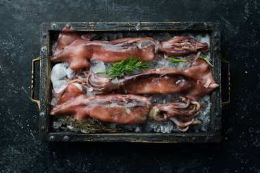 Koyu taşlı arka planda buzlu bir kutuda taze mürekkep balığı. Karanlık bir arka planda.