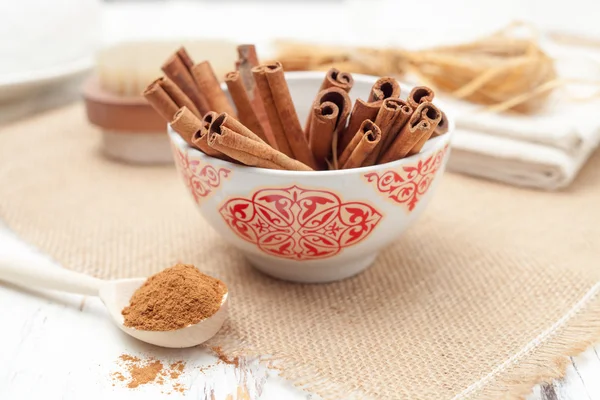 Canela molida en cuchara de madera y palitos de canela en bac blanco — Foto de Stock