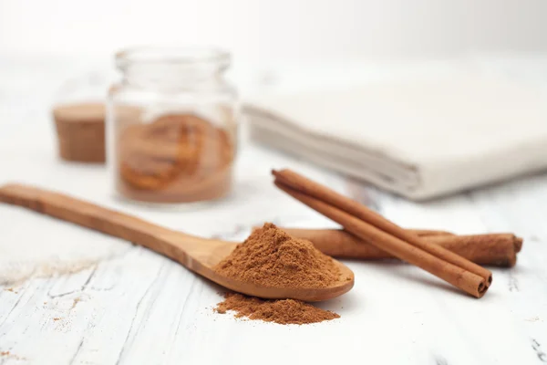 Canela moída em colher de madeira e paus de canela no bac branco — Fotografia de Stock