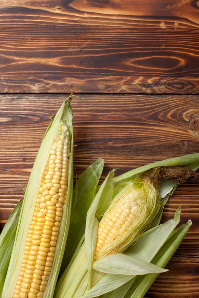 Raw cobs of young corn with leaves on a wooden table — Stock Photo, Image