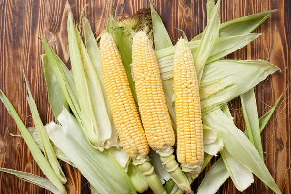 Raw cobs of young corn with leaves on a wooden table — Stock Photo, Image