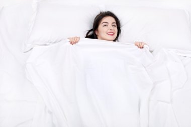 Üstten Görünüm fotoğraf güzel karışık ırk kızın büyük beyaz yatakta yatıyordu. Pijama giyen genç güzel kadın. Arkasında yatan, kendini battaniyeyle kapsayan ve kameraya bakarak kız