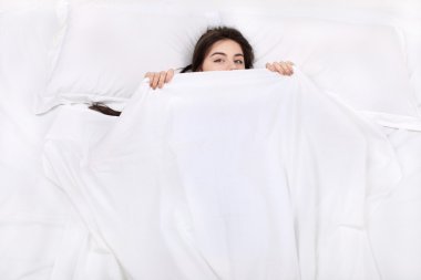 Üstten Görünüm fotoğraf güzel karışık ırk kızın büyük beyaz yatakta yatıyordu. Pijama giyen genç güzel kadın. Arkasında yatan, kendini battaniyeyle kapsayan ve kameraya bakarak kız