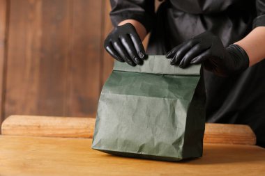 Siyah eldivenli bir el, kağıt bir çanta tutar.