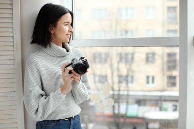 Pencerenin yanında duran kameralı güzel bir hippi kızın portresi.