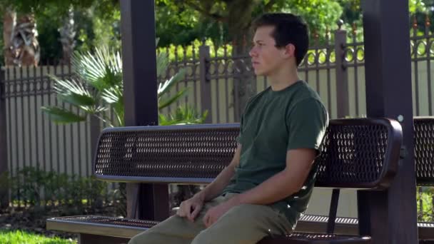 Мужчина сидит на скамейке и проверяет телефон — стоковое видео