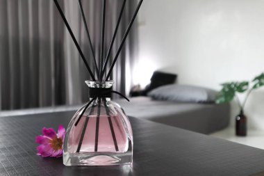 Gri yatak odasındaki siyah masada çiçek serpiştiren şık aromalı sazlıklar.