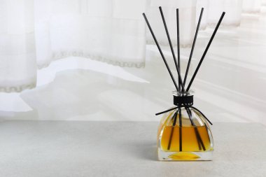 Beyaz perdenin yanındaki beyaz yatak odasındaki gri masanın üzerinde lüks kokulu sazlık cam dağıtıcı.