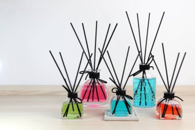 Lüks cam aromalı difüzyon çubuğu beyaz yatak odasındaki ahşap masada mavi, pembe, kırmızı, yeşil renkli yağ sergileniyor.