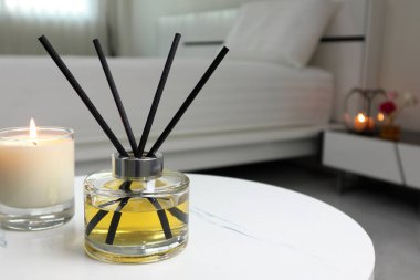 Yatak odasındaki mermer masanın üzerinde oda spreyi olarak sazlık cam şişesinin lüks aromatik kokusu kullanılıyor. Sabahları pencereden ve beyaz yataktan gelen ışığın arka planıyla ortam yaratmak için.