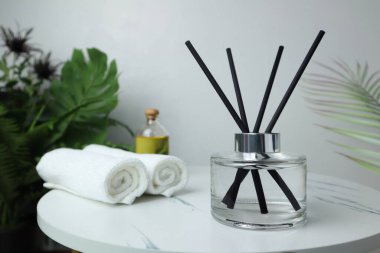 Lüks aromalı kamış aromalı cam şişe spa havluları ve masaj yağı ile mermer masanın üzerinde beyaz beton duvar arka planına sahip beyaz beton kaplıcada oda spreyi olarak kullanılır.