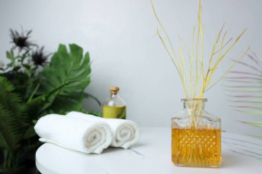 Lüks aromalı kamış aromalı cam şişe spa havluları ve masaj yağı ile mermer masanın üzerinde beyaz beton duvar arka planına sahip beyaz beton kaplıcada oda spreyi olarak kullanılır.