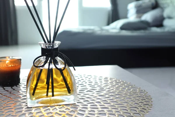 luxury aromatic scent of reed diffuser glass bottle is used as room freshener on the grey table in the bedroom with a scented candle with background of the grey bed in the morning