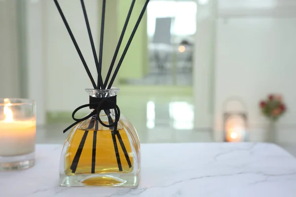 luxury aromatic scent of reed diffuser glass bottle is used as room freshener on the marble table with scented candle in the bedroom with background of the light from the window in the morning