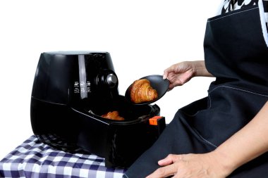 right hand of lady model puts the croissant into the black oil - free air fryer machine on the table in the white kitchen cement wall background clipart