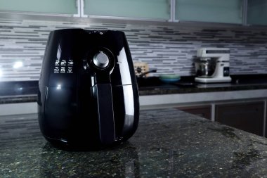 a black deep fryer or oil free fryer , air fryer appliance, is on the black marble table in the nice interior design kitchen of the house clipart