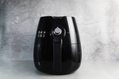 Mutfaktaki çimento duvarlı gri masada, yağsız siyah bir fritöz var. )