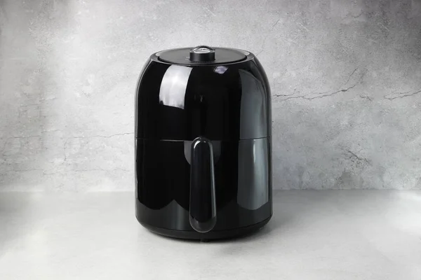 black deep fryer oil free appliance is on the grey table with the cement wall backgroud in the kitchen of the house ( air fryer )