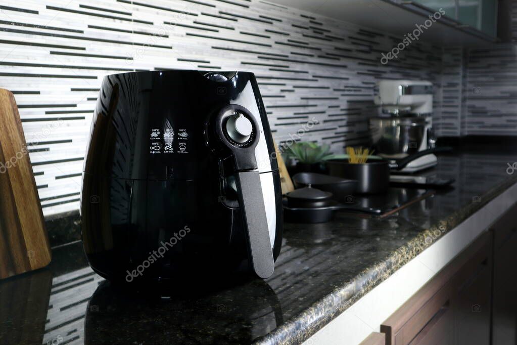 a black deep fryer or oil free fryer , air fryer appliance, is on the black marble table in the nice interior design kitchen of the house