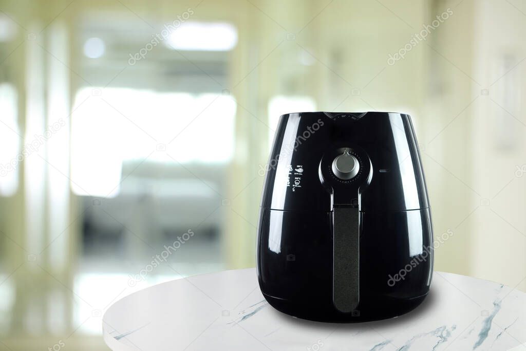 the black air fryer or oil free fryer appliance is on the white marble table with background of the nice kitchen in the morning