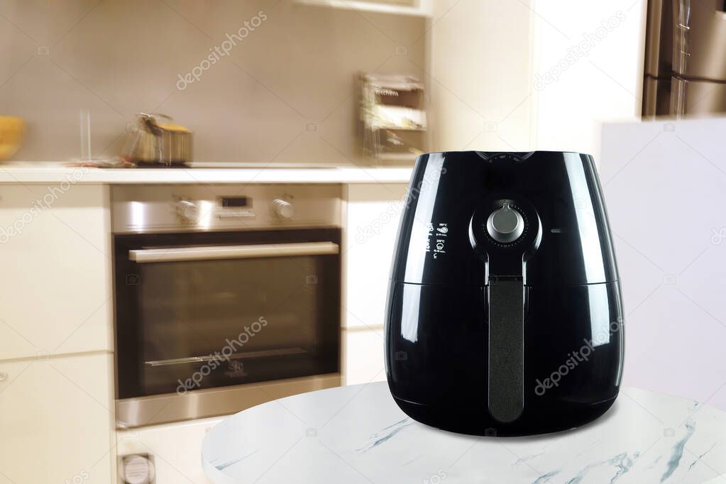 a black deep fryer or oil free fryer , air fryer appliance, is on the white marble table in the nice interior design kitchen of the house during the cooking dinner for family member in Christmas party