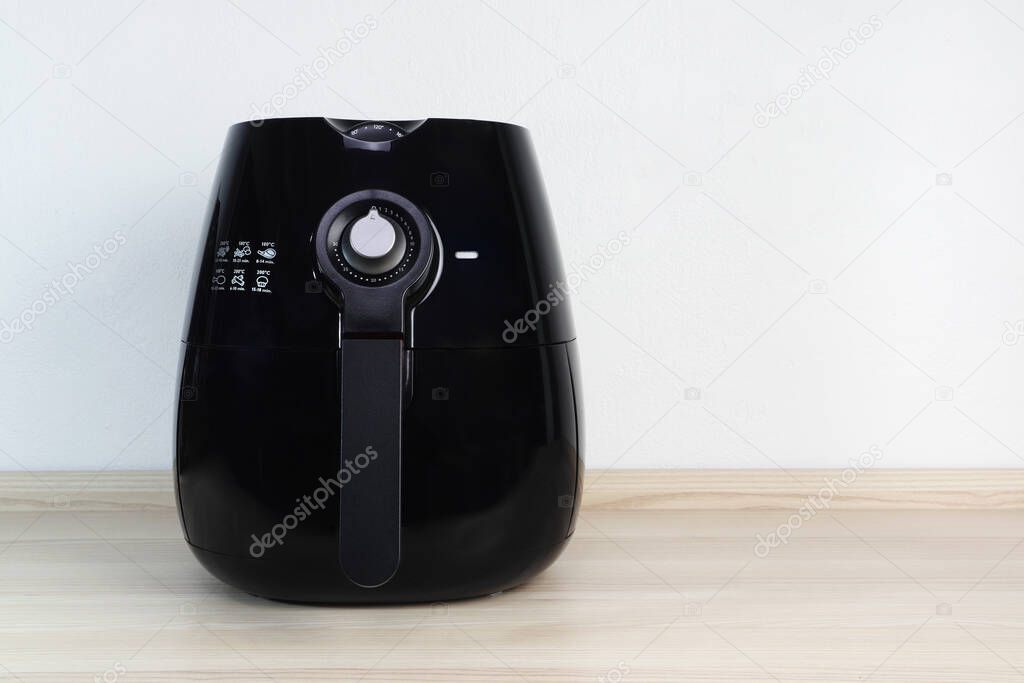 a black deep fryer or oil free fryer appliance is on the wooden table in the kitchen ( air fryer ) with background of white cement wall