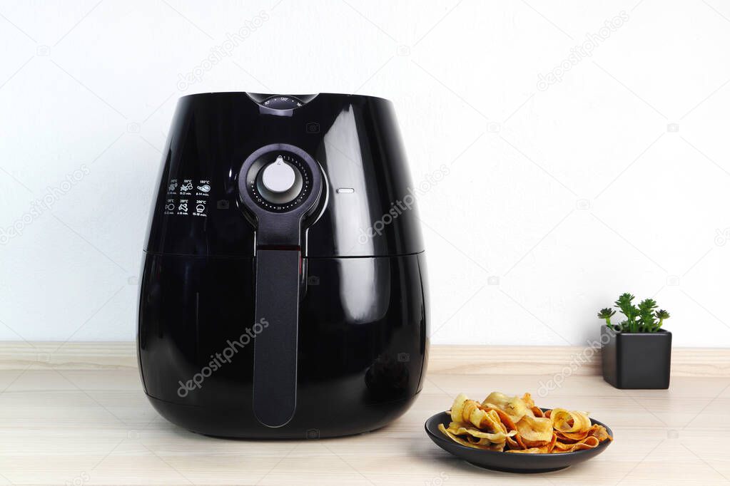 a black air fryer or oil free fryer appliance is on the wooden table in the kitchen with deep fried banana chips and small plant in the pot ( air fryer ) during dinner with happy family member in home
