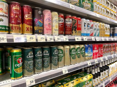 Süpermarket raflarında çeşitli bira markaları sergilenirken renkli teneke kutular ve şişeler Chang, Leo, Singha ve Cheers yer alıyor. resim bira seçeneklerinin çeşitliliğini ve güzel bir perakende satış mağazasının ambalajını temsil ediyor
