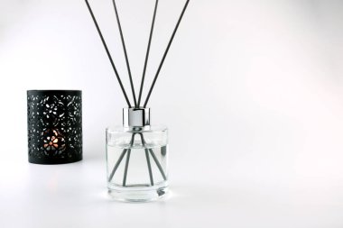 Beyaz masa üzerinde siyah çubuklar ve güzel oturma odasında mum tutucu arka planı olan lüks kokulu kamış kokulu cam şişe oda parfümünden rahatça koku yayabilir.