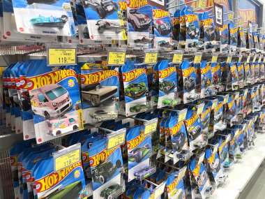 Hot Wheels oyuncak arabalarıyla dolu vitrin rafı sıralı dizilimleri gösteriyor. Parlak ambalaj ve canlı renkler, kolleksiyoncu için görsel olarak çekici perakende sahnesi yaratan minyatür araba modellerini vurguluyor