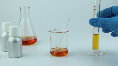 Kimyasal bilim test tüpü, deney tüpü, beher ya da matara beyaz masa üzerinde kullanılan kaplama kağıt parfüm şişesi ve laboratuvarda parfüm ve mum yapımında kullanılan gerekli yağ şişesi.