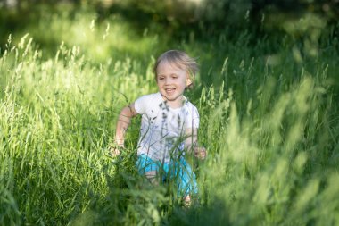 Çocuk uzun yeşil çimenlerde koşuyor..