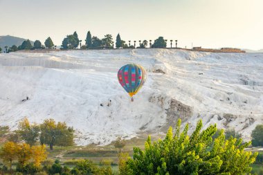 Türkiye 'deki Pamukkale' nin beyaz dağlarının arka planında güzel renkli sıcak hava balonu. Kalsit sarkıtlı teraslı banyolar..