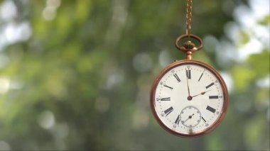 Pocket Watch on Chain Time 4K döngüsünde elleri dönen ve ileri geri sallanan arka planda rüzgarda savrulan bulanık yapraklı altın bir cep saati var.