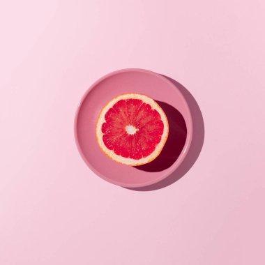 Pastel pembe bir çay tabağının üzerine pembe bir fonda duran parlak kırmızı bir greyfurt. Düz yatıyordu. Asgari konsept.