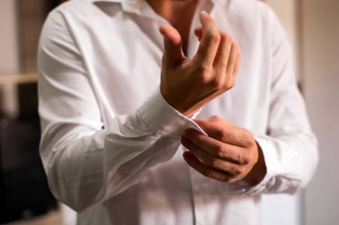 Beyaz gömleğinin düğmelerini elleriyle ilikleyen bir adam.