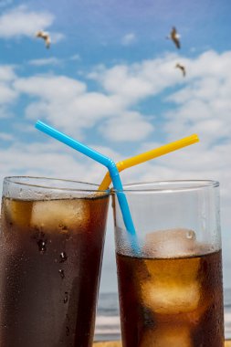 Kanarya Adaları, Tenerife 'de mavi gökyüzü ve uçan martılarla plajda buzlu ve pipetli iki bardak soda yakın plan. İspanya