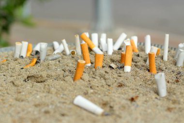 Sigara izmaritleri kül tablasına sıkışmış. Sokakta bir kum var. Yakından seçici fokus..