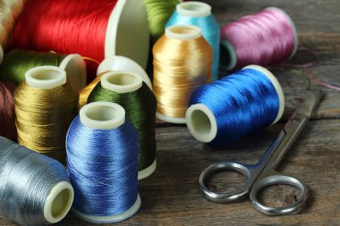 Ahşap zemin üzerinde renkli iplikler ve makaslarla bobbin, yakın plan, seçici fokus