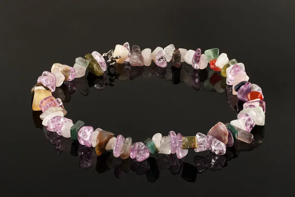 Крупный план ожерелья из кристаллов аметистов, флюорита, яшмы и розового кварца на черном столе — стоковое фото